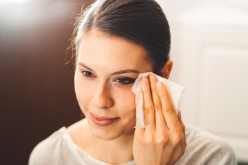 Young caucasian woman clenaing off her make up with a cotton pad late at night in her bathroom 