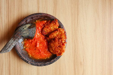 Red chili sauce and tomato with Dadar jagung made from corn, flour, and egg placed on a mortar and pestle.