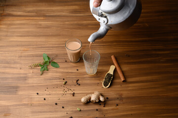 indian masala chai or tea in traditional glasses, with kettle, spices and tea leaves on dark,...
