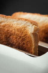 Close-up shot of slightly burnt white bread toasts sticking out of a toaster on the black background. Ready toasts with a dark  crust. Morning breakfast concept