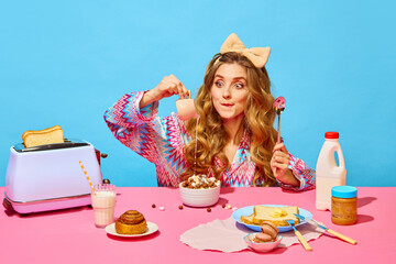 Food pop art photography. Redhead girl with bow preparing milk flakes with hungry eyes on pink tablecloth over light blue background