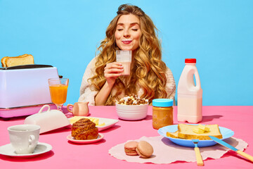 Food pop art photography. Happy beautiful young girl with ginger hair drinking milk over light blue background. Table setting for breakfast - obrazy, fototapety, plakaty