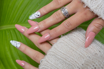 close-up of two hands with pink sculpted nails and a background of green leaves