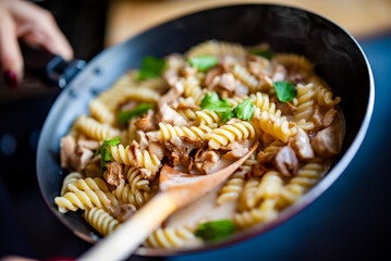 cooking tasty chicken fillet with mushroom in a creamy sauce with fusilli pasta in pan on kitchen