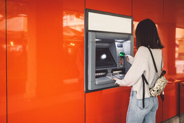 Woman inserting her card in the ATM machine, making a cash withdrawal 