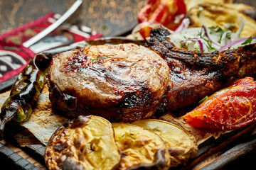 Pork steak on the bone, barbecued with vegetables on a wooden board. Close up