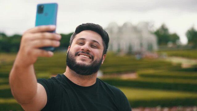 Handsome young man smiling while taking a selfie at a park outdoors located at Botanical Garden, Curitiba, Brazil