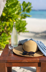 Glass bottle of water, straw hat and sun glasses on the background of the beach in the Maldives