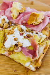 Due fette di Pinsa Romana condite con con pancetta, burrata, patate e tarallo sbriciolato e con prosciutto cotto, crocchè di patate e mozzarella poggiate su un tagliere di legno