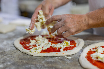 Pizzaiolo napoletano mentre condisce una pizza Margherita tradizionale napoletana con mozzarella di bufala sul banco da lavoro in marmo di una pizzeria napoletana 