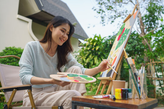 Creative art concept, Female artist is washing paintbrush while painting art on canvas in garden - Powered by Adobe