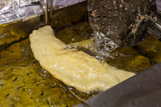 Pizza fritta napoletana ripiena di ricotta e cicoli di maiale in cottura nell'olio bollente 