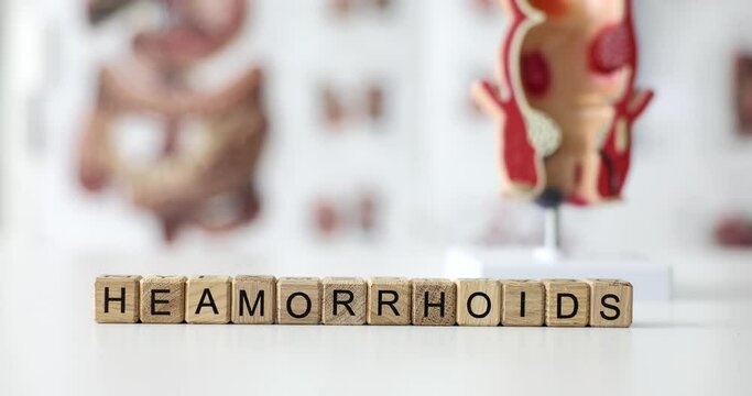 Word hemorrhoids on wooden cubes on background of model of rectum and poster 4k movie