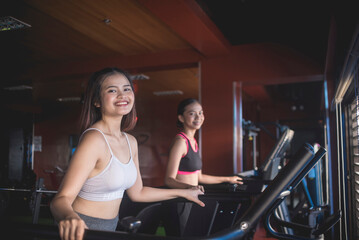 Obraz premium Two pretty asian women smiling while brisk walking on the treadmill. Working out or doing cardio inside the gym.