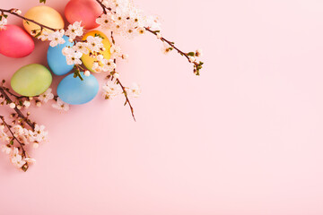 Happy Easter. Dyed Easter eggs on rustic table with cherry blossom tree branch on pink background. Easter holiday card background with copy space. Top view.
