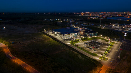 Fototapeta premium Aerial view of the shops next to bigger highway with many cars and forest in the historical and at same time modern city of St. Petersburg at summer night