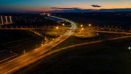 Fototapeta na wymiar Aerial view of the bigger traffic interchange with many cars next to forest and the historical and at same time modern city of St. Petersburg at summer night