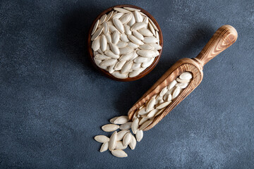 A bowl with spoon full of pumpkin seeds,on dark background
