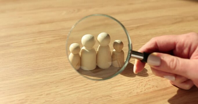 Hand holding magnifying glass over family of wooden men closeup 4k movie