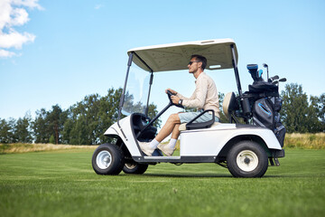 Full length side view of man driving golf cart across green field in sports club, copy space