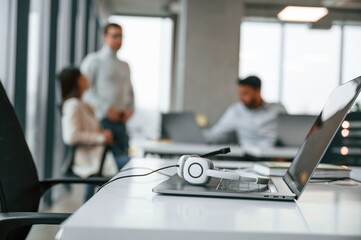 Fototapeta premium Headphones is lying down on the laptop. Men and woman are working in the office together