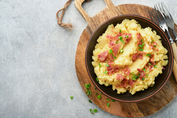 Mashed boiled potatoes. Bacon mashed potatoes with green onion, pepper and cheddar cheese in bowl on light old wooden backgrounds. Delicious creamy mashed potatoes. Top view.