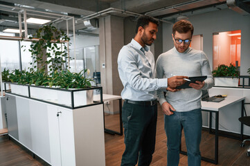 Information in the tablet. Two men are working in the modern office together