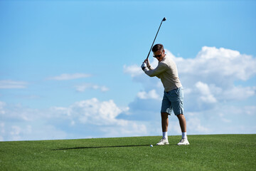 Full length portrait of active sporty man swinging golf club on field against blue sky, copy space