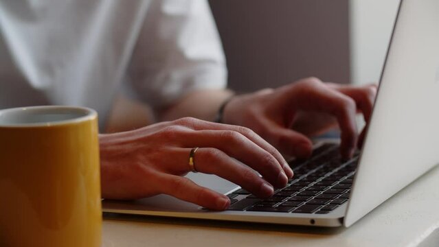 Cropped view of a man remotely working on a laptop from a cafe. A man is typing on a laptop keyboard and running his fingers over the touchpad.