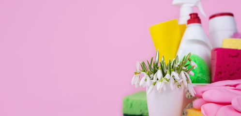 Spring cleaning concept. Snowdrops and detergents and cleaners for cleaning the house on a pink background. Banner. Copy space. Close-up. Selective focus.
