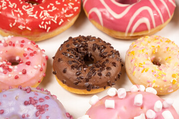 Many different donuts on a white background top view, pink, white and chocolate donuts of different sizes