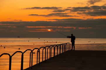 Beautiful sunrise and one alone fisherman near the sea.Silhouette of a man fishing on pier at sunset, Marsaskala, Malta