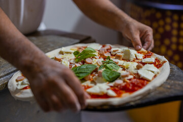 Pizza tradizionale napoletana condita con sugo di pomodoro, würstel, mozzarella di bufala e basilico fresco mentre viene stesa sulla pala di una pizzeria napoletana e pronta per essere infornata