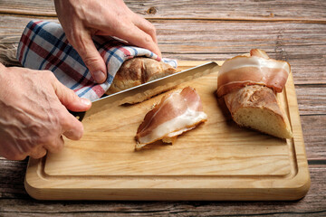 chef cuts fresh bread for making bacon sandwich