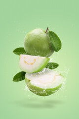 Creative layout made form whole and slice of Guava fruit and water splashing on a green background.