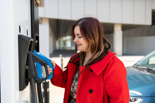 Young woman taking electric car charger plug