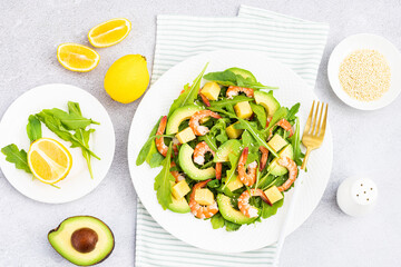Flat lay of Healthy salad plate. Fresh seafood recipe. Grilled shrimps and fresh vegetables (avocado, arugula, mango) on gray concrete background. 