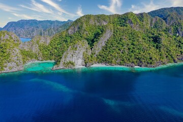 Naklejka na ściany i meble Panorama drone shot of majestic rocks in Coron, Palawan in the Philippines, covered with bushes and surrounded by the sea.