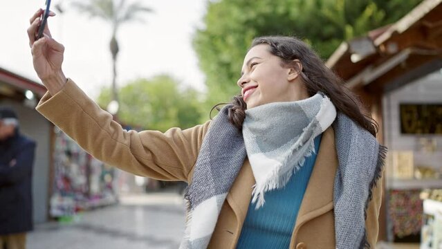 Young beautiful hispanic woman smiling confident making selfie by the smartphone at street market