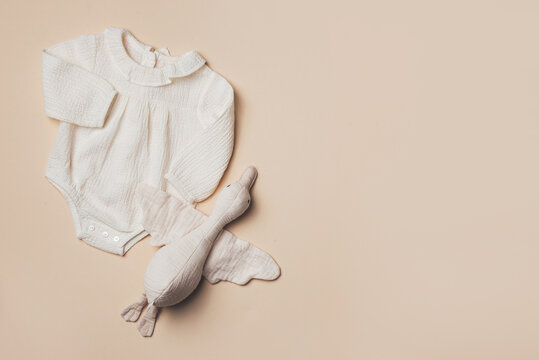 Mockup of cream infant bodysuit made of organic cotton with eco friendly baby accessories, soft duck on beige backgroundd. Gift for newborn baby. Top view. Flat lay. Copy space