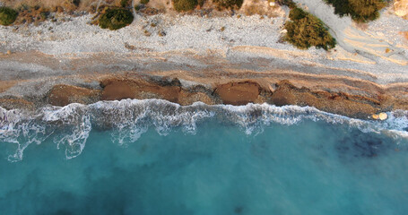 Flying drone over the coastline of the island overlooking rocky shoreline with vegetation and rocks and clear sea with light foamy waves in Cyprus.