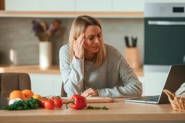 Tired, having headache. Beautiful young woman is on the kitchen