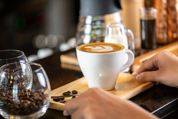 White ceramic cups of cappuccino with latte art Barista make coffee by pouring spills hot milk cream on black coffee. Barista serve holding cup of hot latte and coffee beans on wooden table cafe shop