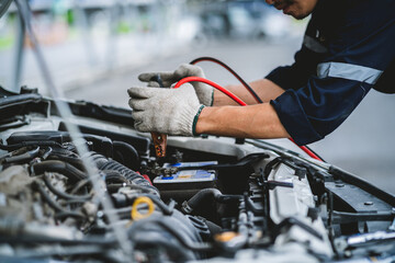 Asian technician measures car battery voltage at service station Maintenance and repair. The...