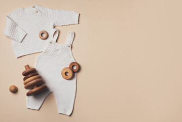 Newborn beige romper, sweater, pants, shoes, wooden toys on neutral backgroundd. Set of knitted baby clothes. Top view, flat lay. Copy space. Fashion baby clothes outfit and accessories collection