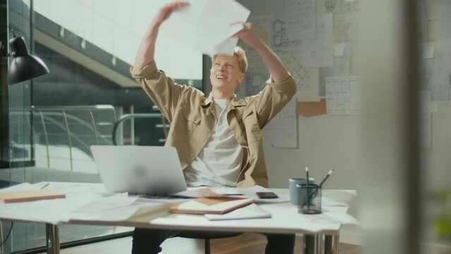 Engineer Bursting with Joy Reviewing Documents. Successful Man Making Profitable Deal and Celebrating the End of the Project.Young Smiling Architect Scatterring Papers around Him Waving Fists Happily