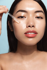 Asian young woman with skin hydrating serum, holds dropper with cleanser, treating her natural...