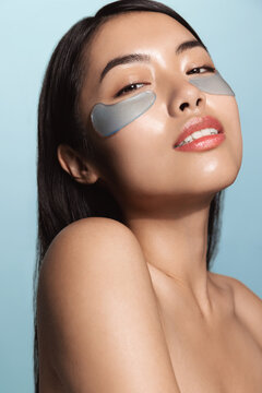 Woman no makeup, natural face, using under eye paches for skin nourishment and lifting, removing dark circles with cucumber seed and argan oil active ingredients. Asian girl does skincare routine