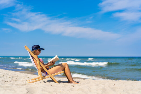 Woman relaxing on beach reading book sitting on sunbed