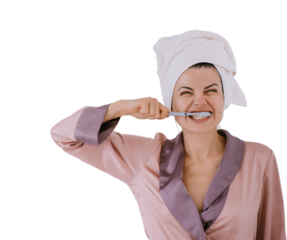 Annoying young adult woman in silk robe and towel wrapped around head brushing teeth against transparent background. Hygiene and morning routine. Caucasian female in rush preparing to go outside.